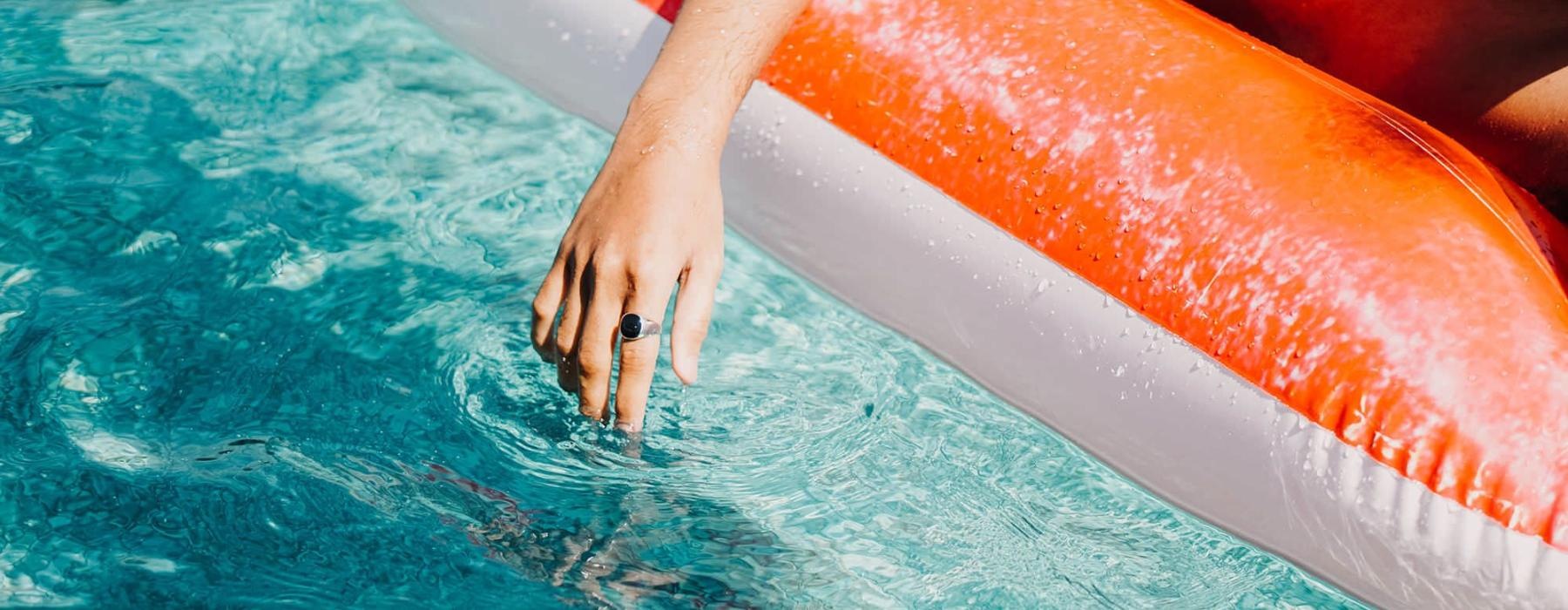 woman dangles her hand in the pool as she floats in an inflatable vessel